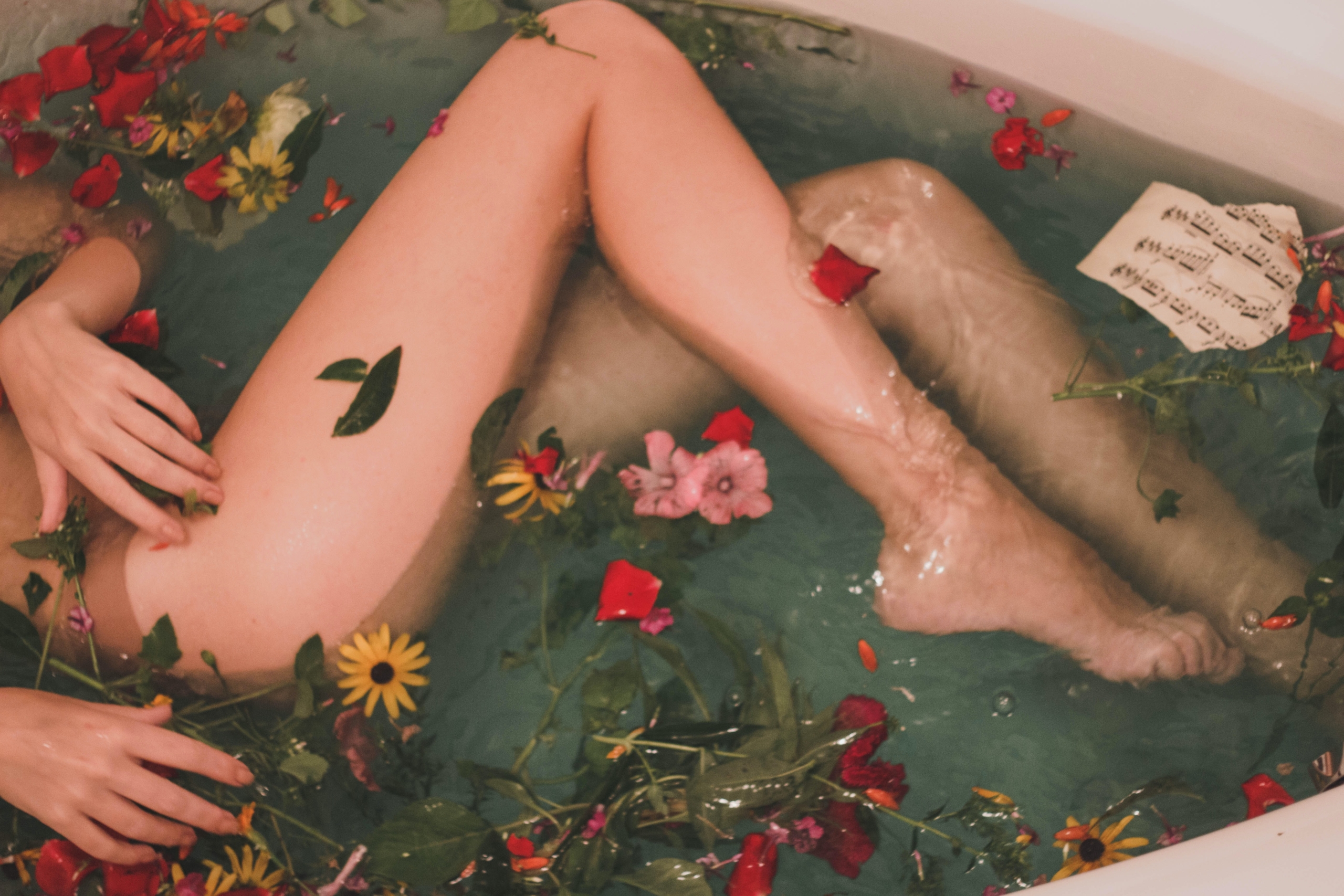 corpo femminile in una vasca da bagno con acqua e fiori
